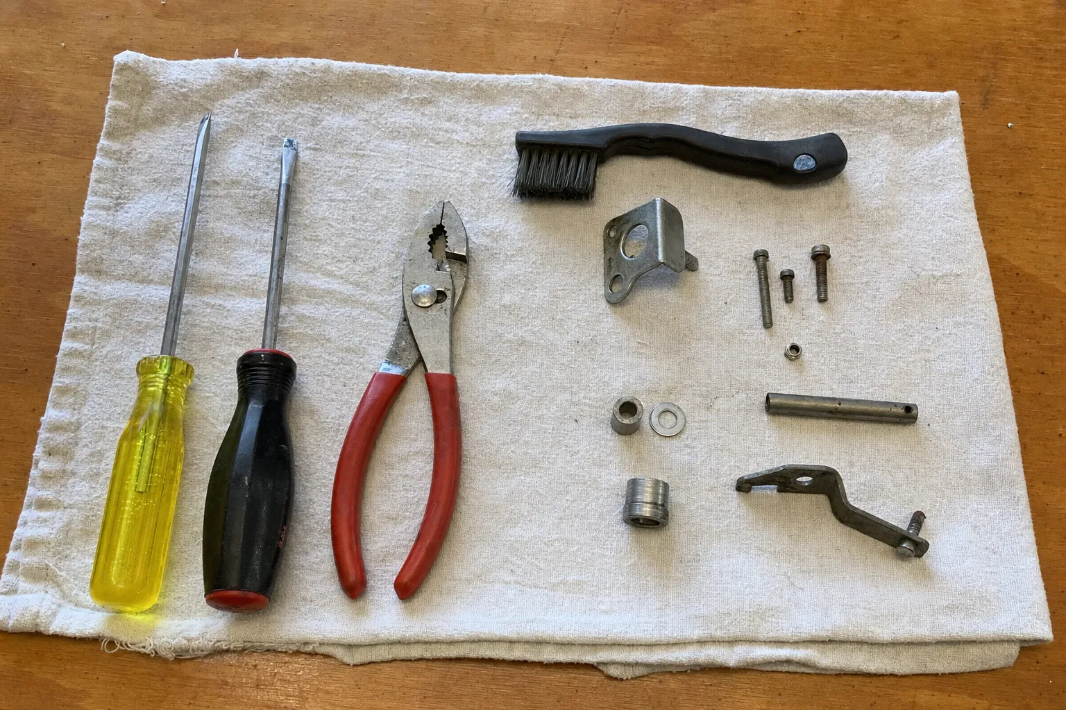 Screwdrivers, pliers, a brush and small replacement parts arranged on a cloth